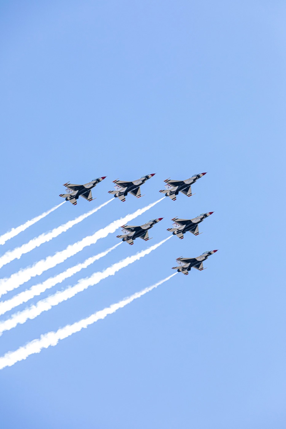 A formation of jet aircraft climbing steeply into a clear blue sky leaving vapour trails