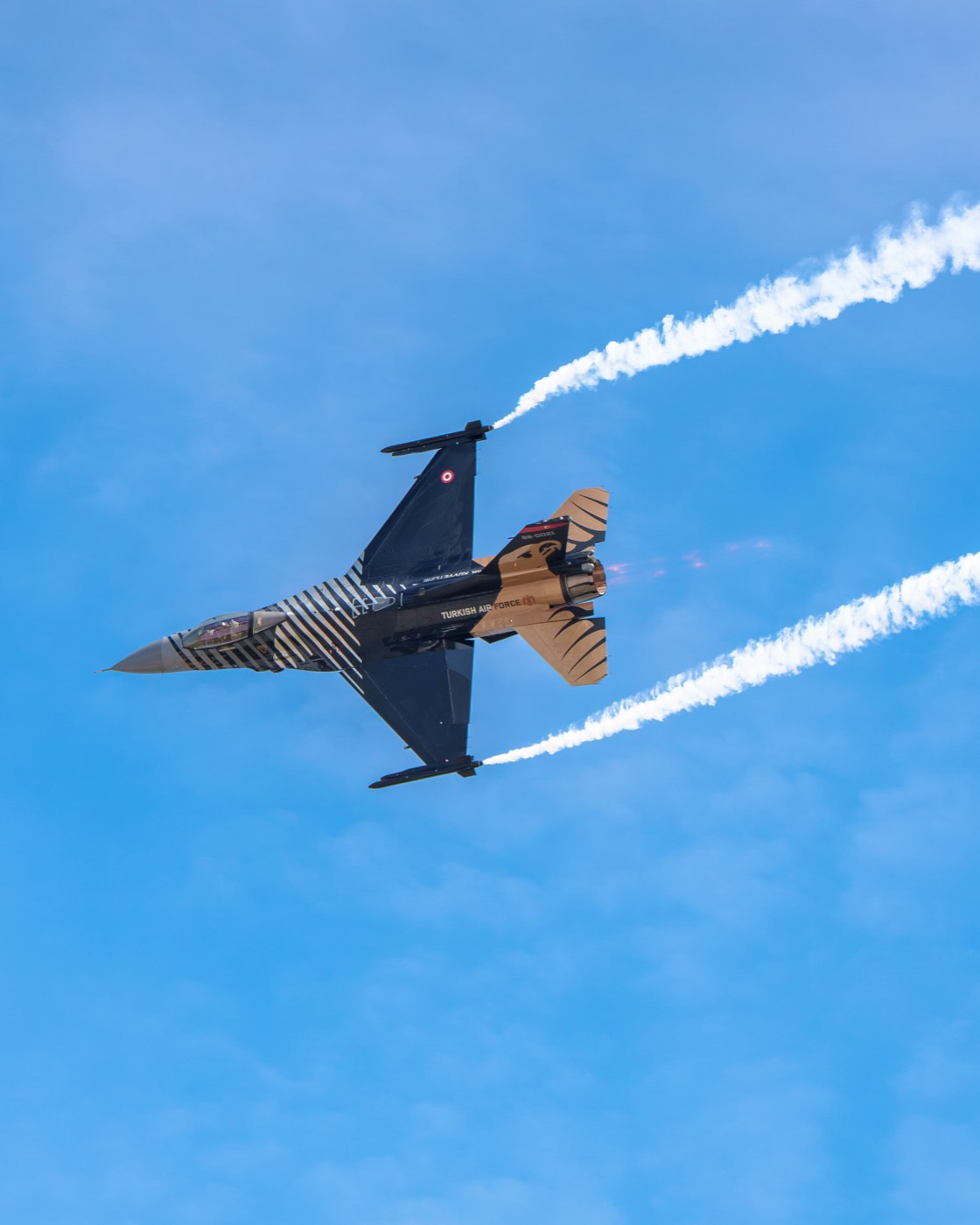 A single fast jet in a banked turn trailing white smoke against a clear blue sky